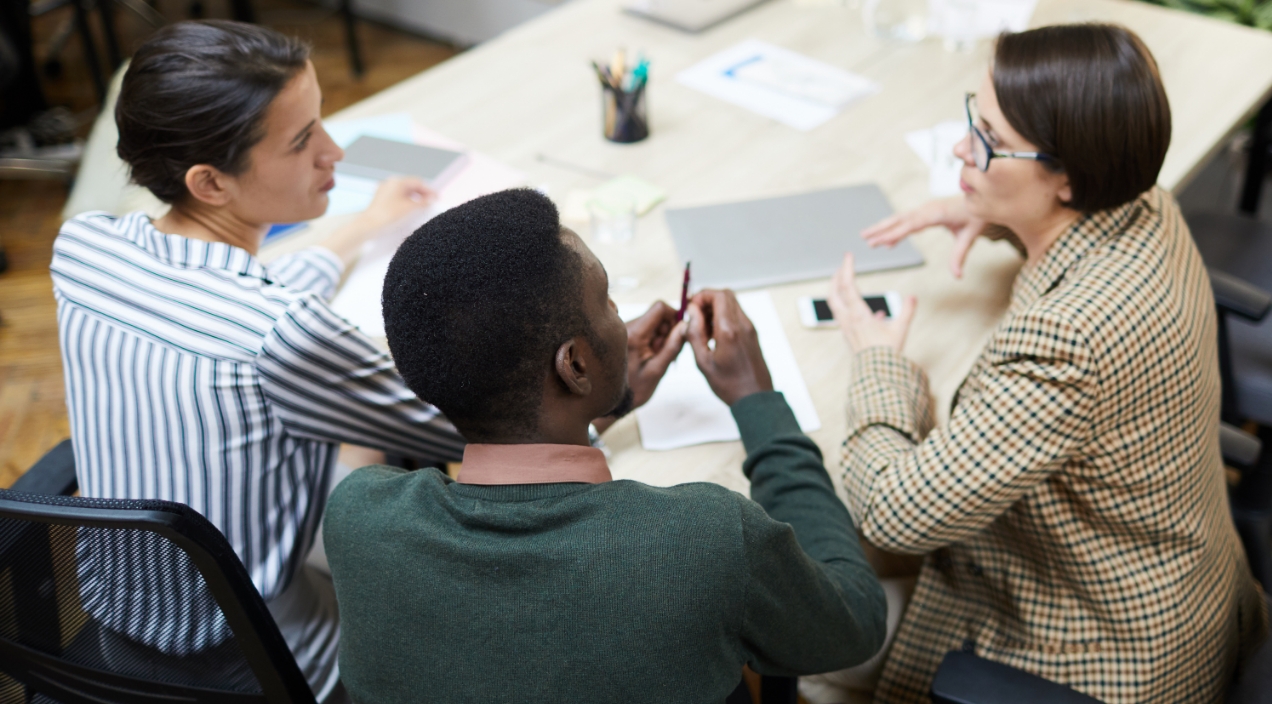 two females and one male in business casual clothing sitting at table in a discussion